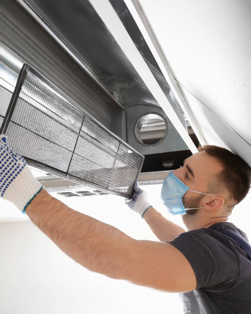 Male technician cleaning industrial air conditioner indoors