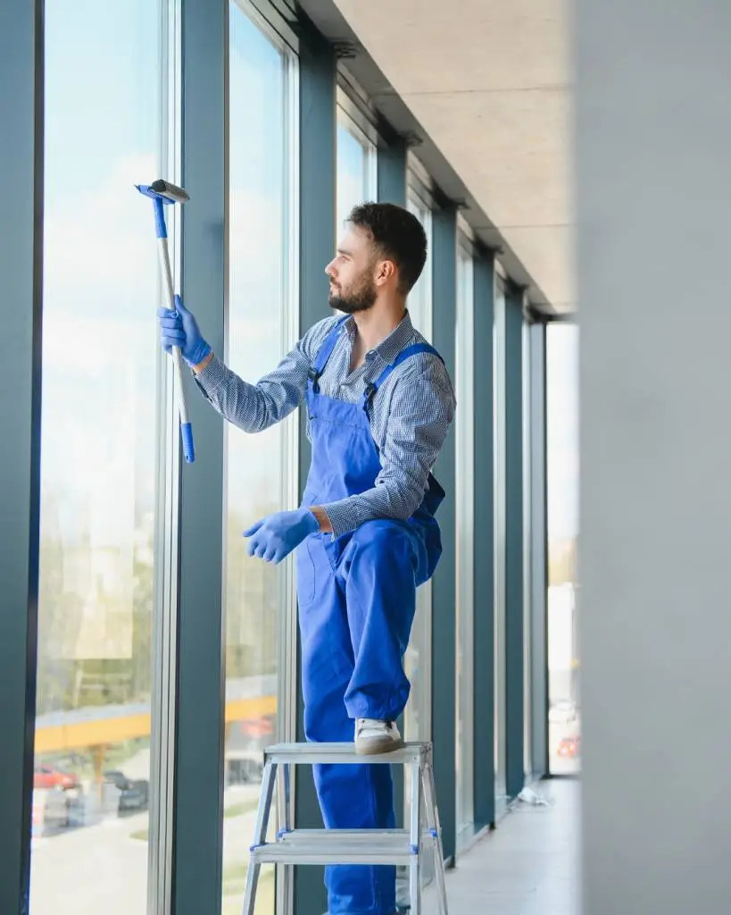 Male janitor cleaning window in office
